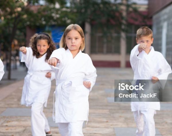 Young children in kimono perform techniques karate on a city street